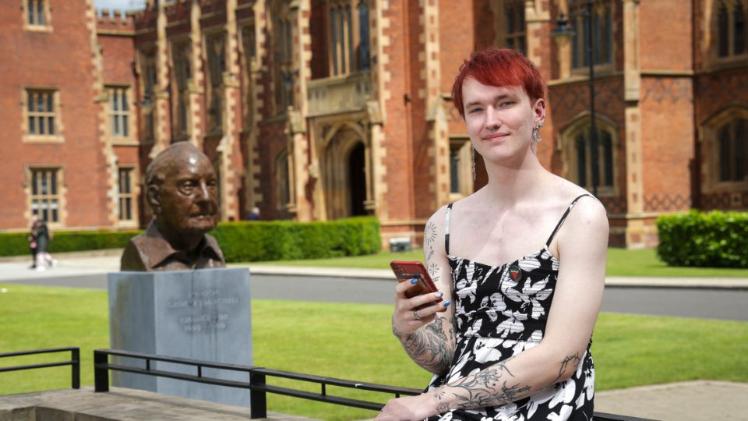 person sitting outside Queen's university Belfast looking at their mobile phone and smiling